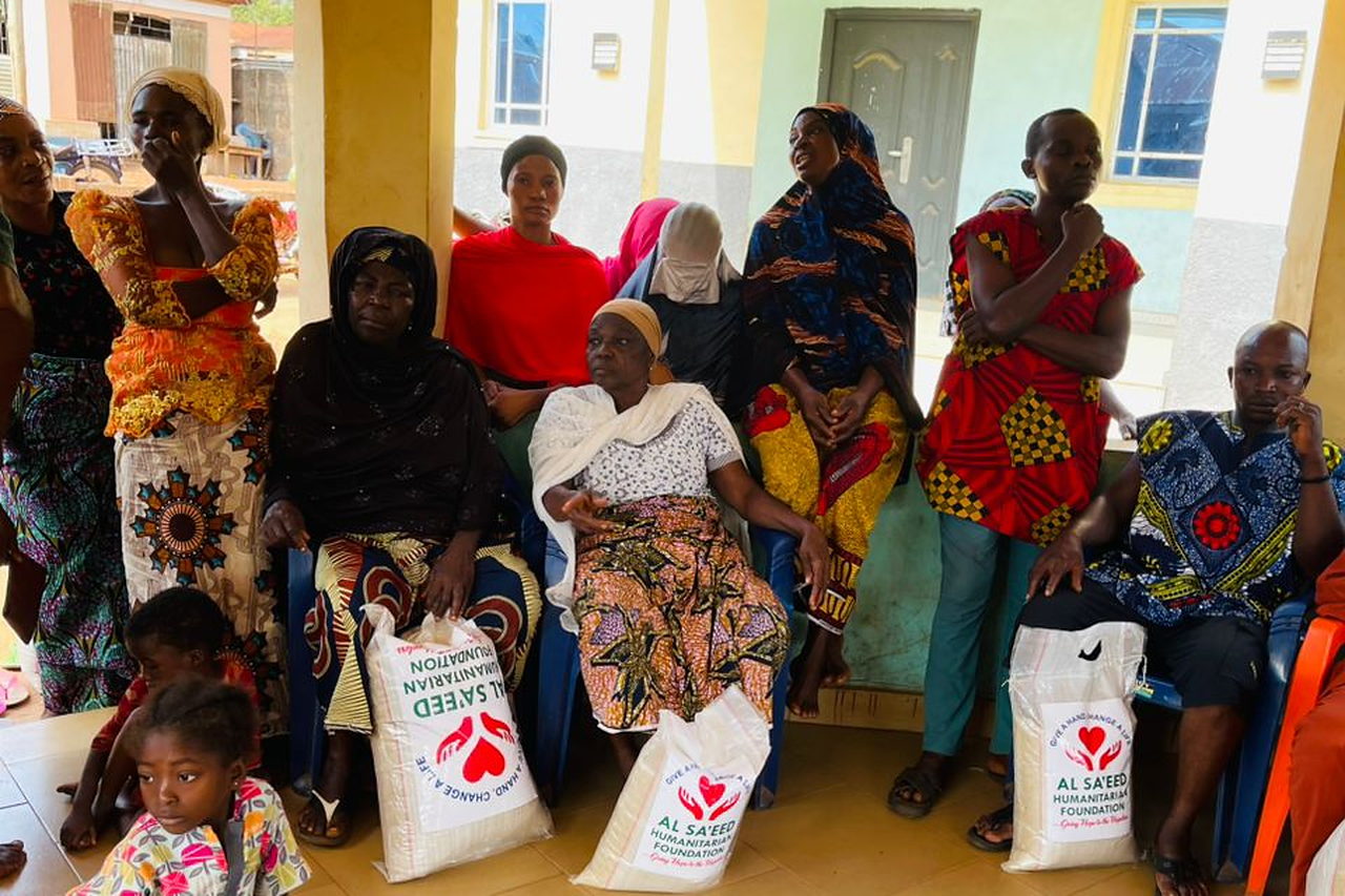 Women and children seated together with Al Sa'eed Humanitarian Foundation relief bags at a community distribution.